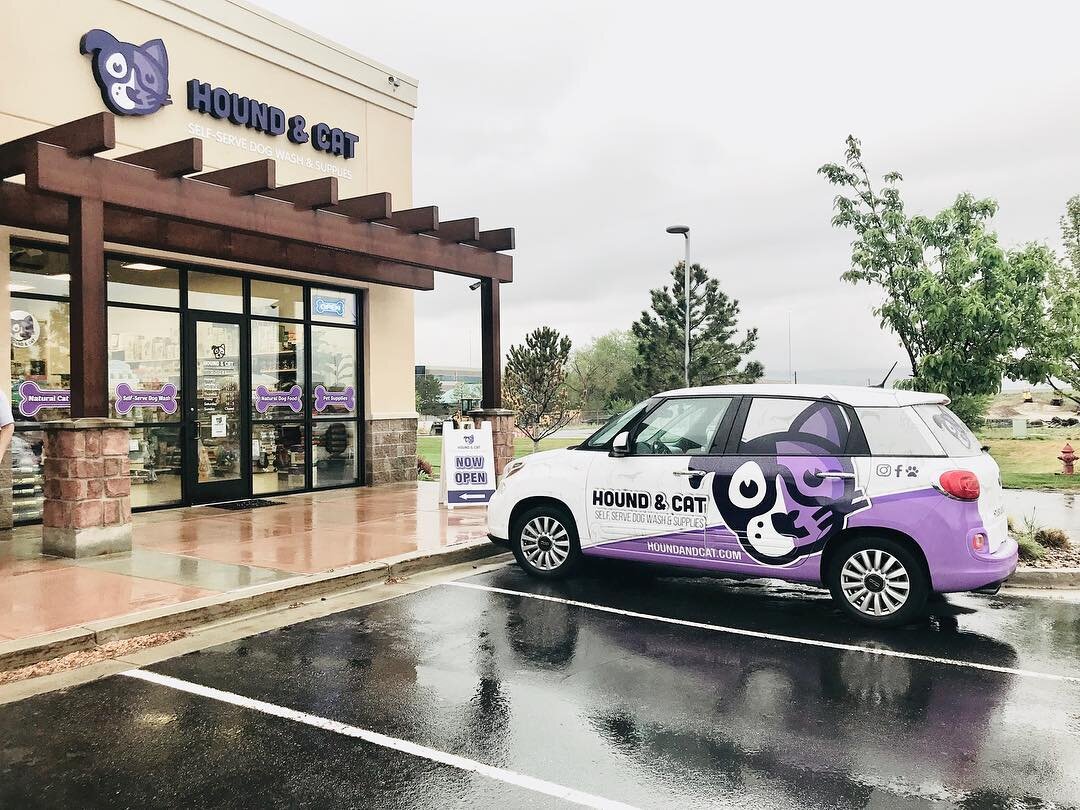 A branded purple and white van featuring a graphic that is half dog face and half cat face sits parked in front of Hound and Cat pet store in Draper on a rainy day