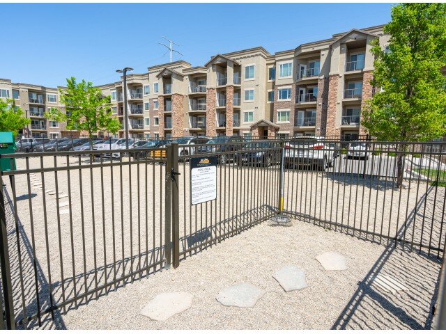 A double gated dog park entrance sits in front of a newer apartment complex