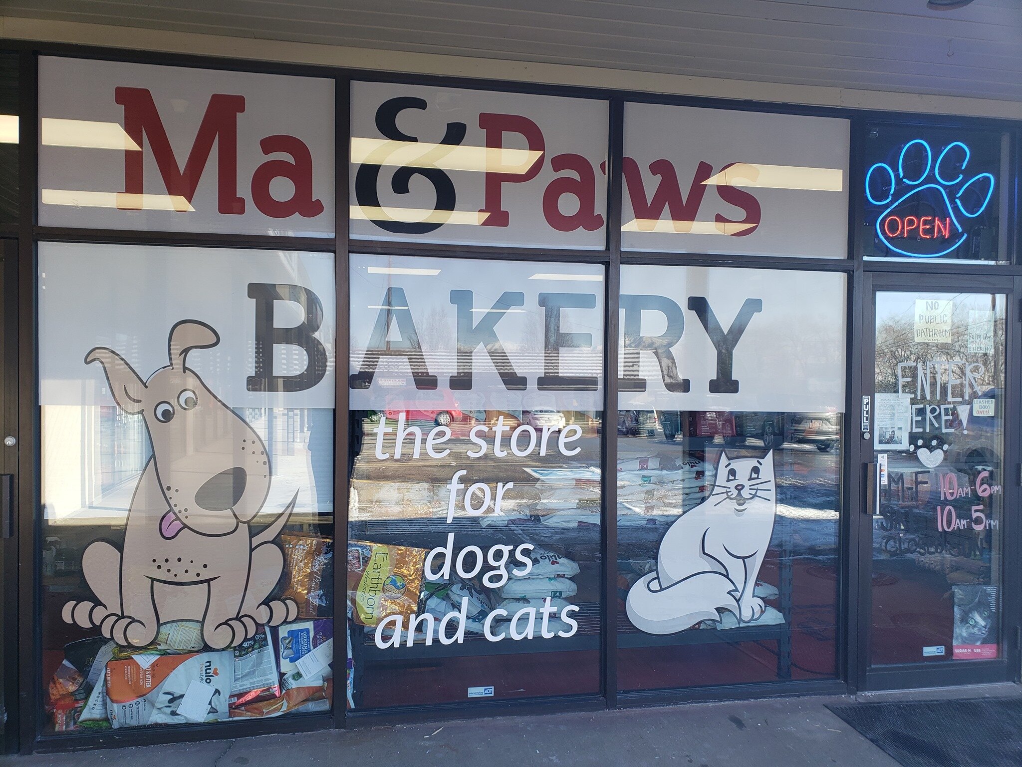 The glass storefront for Ma & Paws Bakery includes a large name sign and cartoon painting of both a dog and a cat