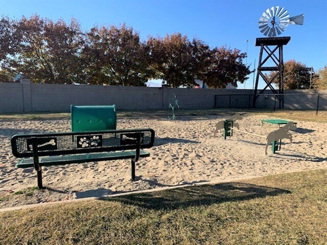 A small, sandy dog park with agility equipment featuring a windmill decoration.